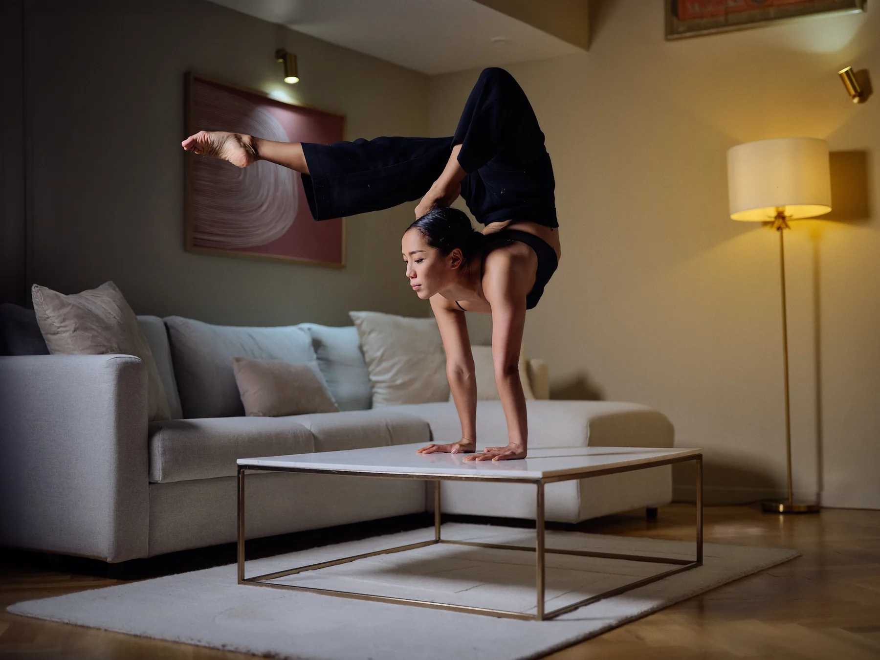 Nyamgerel performing a handstand on a marble coffee table in a warmly lit interior